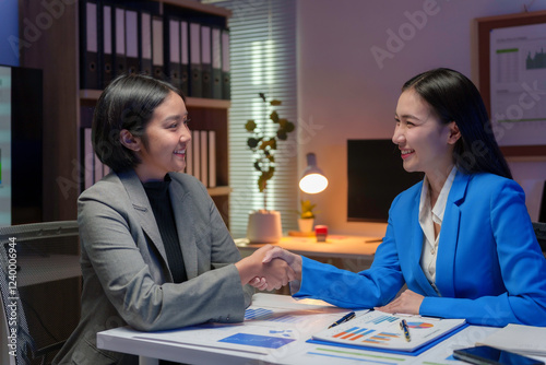 Two happy businesswomen shaking hands after closing a deal in office at night photo