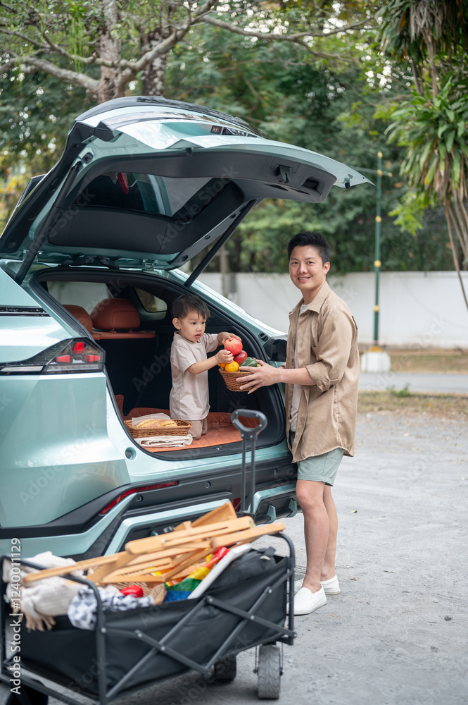 An innocent little Asian boy and his dad are in the trunk of their car, organizing camping gear.