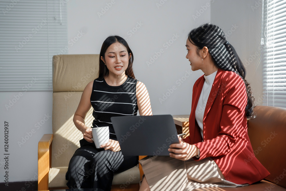 Two businesswomen discussing work using laptop and drinking coffee Two businesswomen discussing work using laptop and drinking coffee
