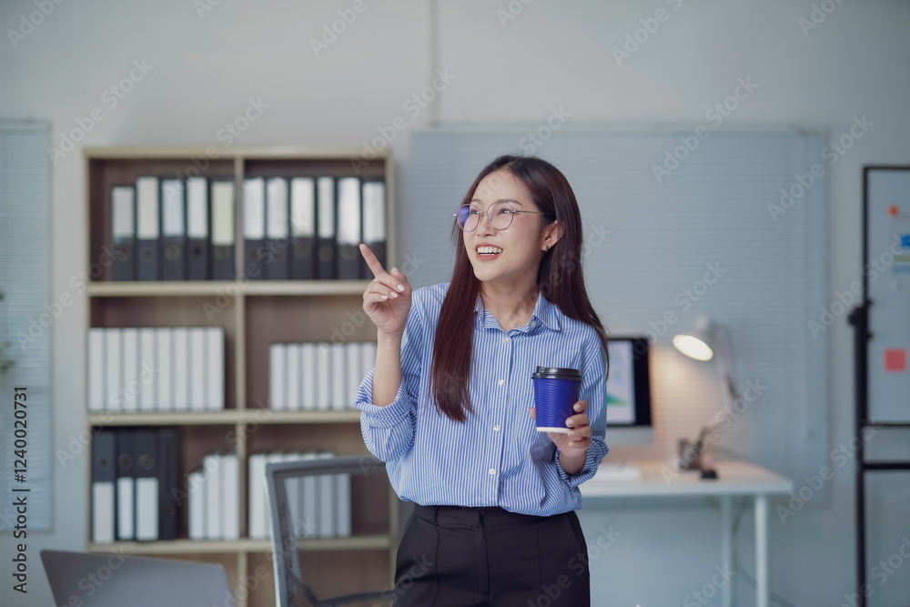Young Asian businesswoman pointing finger and holding coffee cup in office