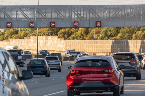 Highway traffic with multiple red 80km/h speed limit signs mounted on an overhead gantry, with various cars driving on the multi-lane motorway.Melbourne Australia.