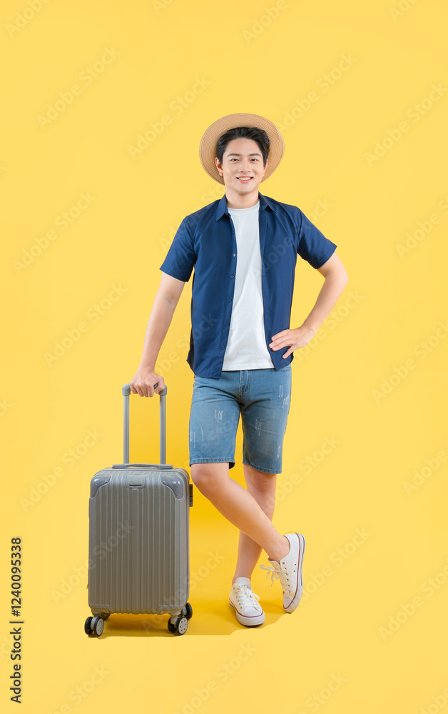 Full body image of a young Asian man pulling a suitcase and posing on a yellow background Full body image of a young Asian man pulling a suitcase and posing on a yellow background