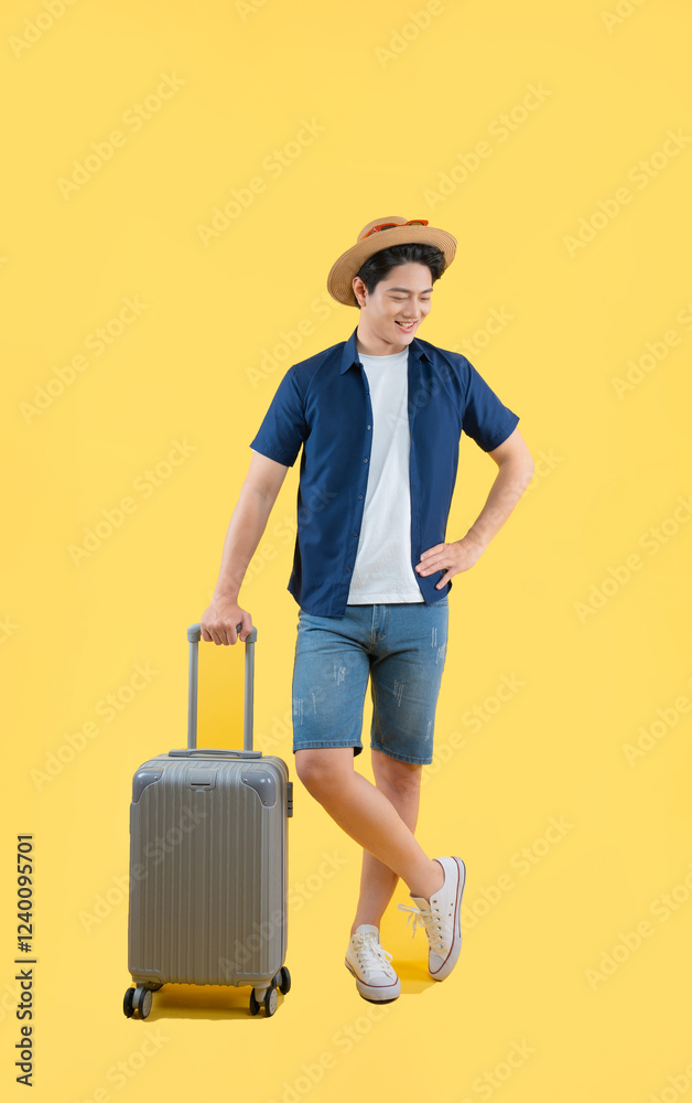 Full body image of a young Asian man pulling a suitcase and posing on a yellow background Full body image of a young Asian man pulling a suitcase and posing on a yellow background