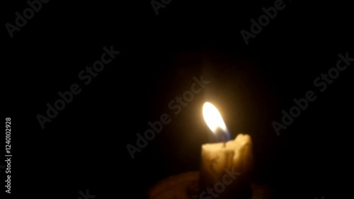 A single candle burns softly in a dark and quiet room, its flickering flame casting moving shadows on the walls. The warm golden glow creates a peaceful and intimate atmosphere, calm and tranquility