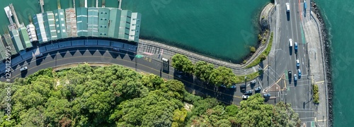 High-angle view of a city street corner meeting a waterfront, with cars and pedestrians. Traffic flows along the curved road, alongside the harbor. BOAT SHEDS, ORAKEI, AUCKLAND, NEW ZEALAND