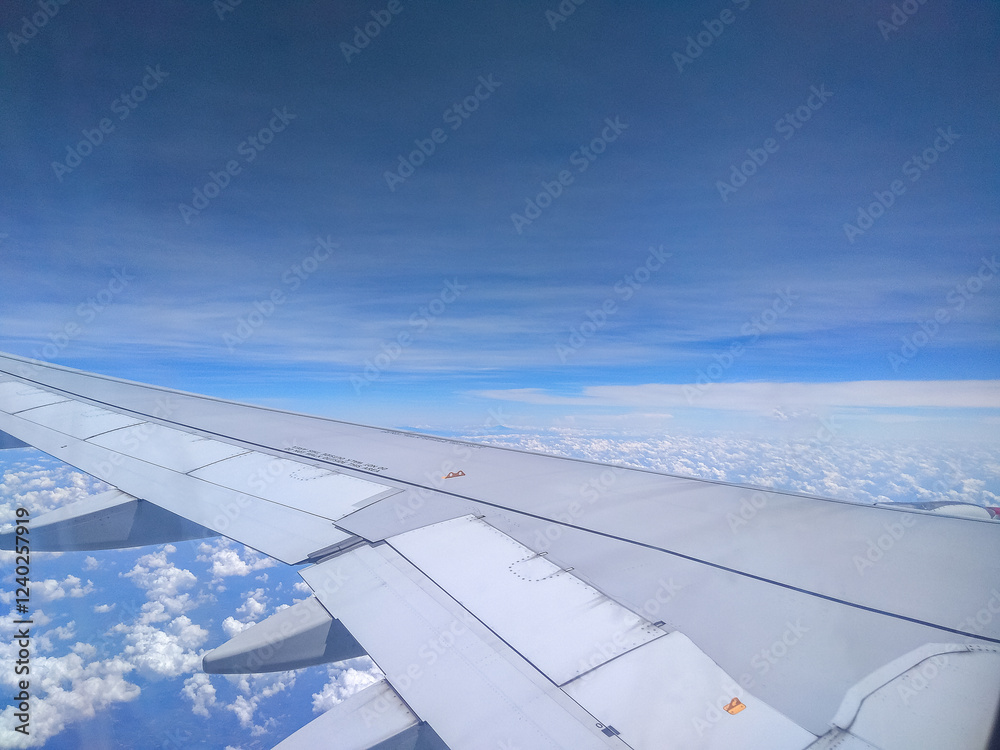Stunning cloudscape seen from an airplane window during flight. Blue sky, white clouds and airplane wing. Aerial View of Cloudscape from Airplane Window Stunning cloudscape seen from an airplane window during flight. Blue sky, white clouds and airplane wing. Aerial View of Cloudscape from Airplane Window