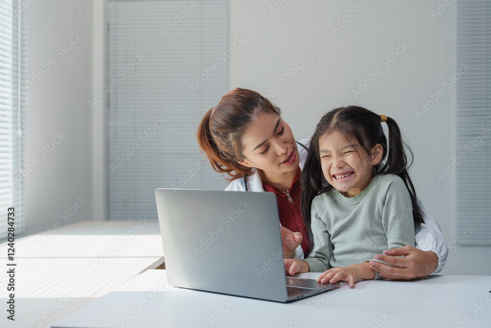 Asian female doctor is showing something funny to a little girl patient on a laptop, making her laugh, during a visit in her bright modern office Asian female doctor is showing something funny to a little girl patient on a laptop, making her laugh, during a visit in her bright modern office
