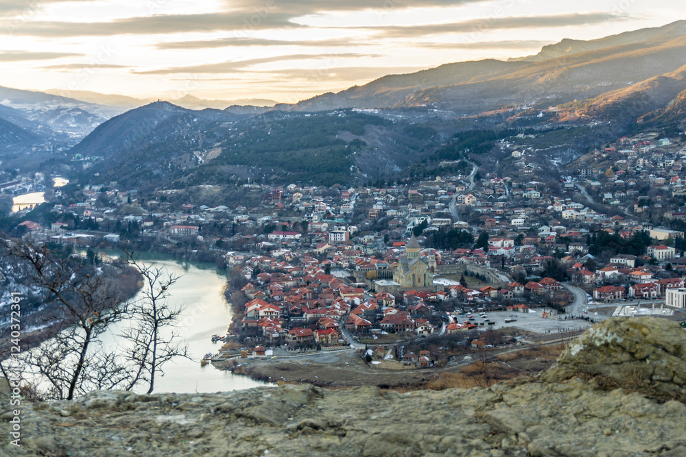 Fototapeta premium View of Mtskheta from Jvari Monastery. The setting sun illuminates the mountains. The clouds are orange. Mountains around