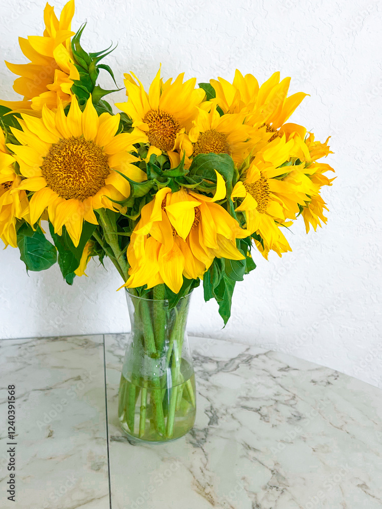 A bouquet of sunflowers stands in a glass vase on a marble table in a white kitchen