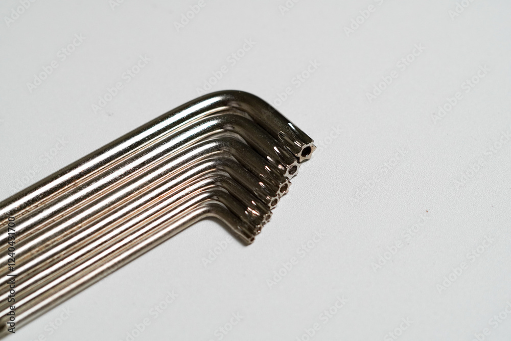 Set of metal L-shaped hex keys with hexagonal ends neatly arranged on a white surface for use. Set of metal L-shaped hex keys with hexagonal ends neatly arranged on a white surface for use.