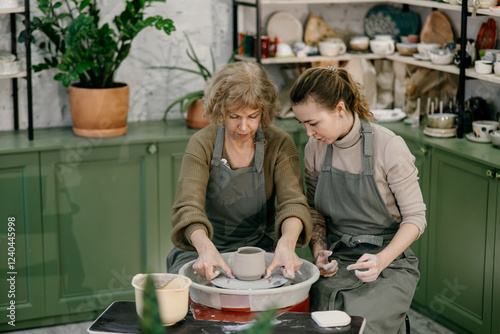 Hands-on learning, senior woman mastering pottery techniques using rotating wheel Mentor teaches pottery fundamentals, demonstrating sculpting skills on an electric wheel photo