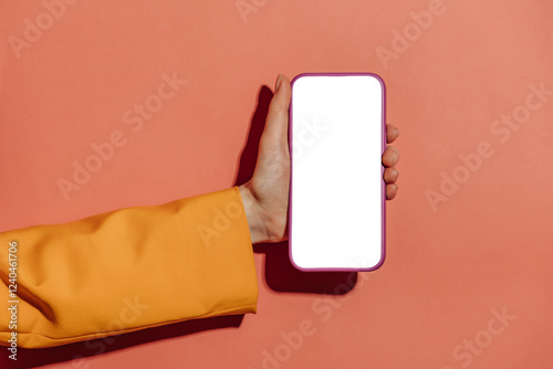 woman's hand in a yellow blazer holds a mobile phone with a white screen mockup against a pink background