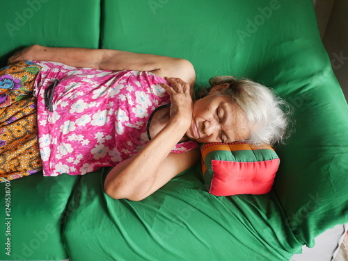 Beautiful Asian elderly blonde woman in pink dress sleeping on a green sofa in her home