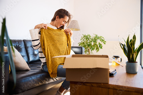 Smiling woman trying on sweater bought online sitting on sofa at home