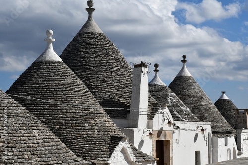 The grey stone and conical roofs of the trulli houses in Alberobello, with white stone wash walls. The sky is overcast with grey clouds. photo