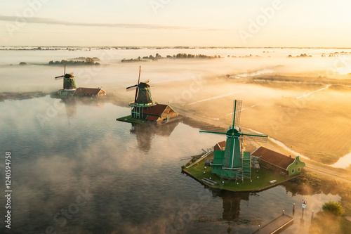 Aerial view of misty windmills reflecting in tranquil water at sunrise, Kalverpolder, Zaandam, North Holland, Netherlands. photo