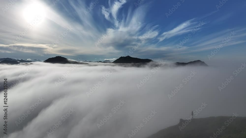 Aerial view of low clouds over majestic mountains with a woman standing on the edge, Unalaska, United States. Aerial view of low clouds over majestic mountains with a woman standing on the edge, Unalaska, United States.