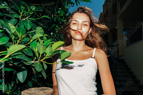 A young woman stands among lush green leaves, her hair flowing in the breeze, exuding confidence and natural beauty photo