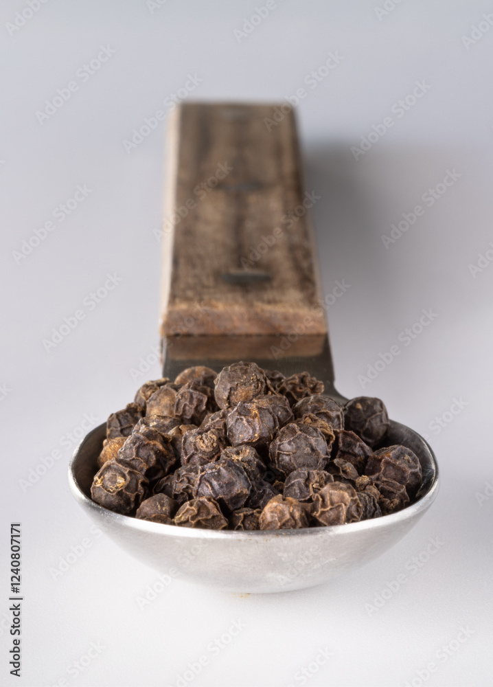 Perspective view of Raw organic black peppercorns or Dry black pepper seeds in stainless steel spoon isolated on the white background. use it as your Space for text, Design, Wallpaper and Poster.