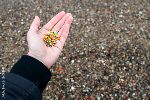 Open palm filled with tiny microplastic particles against sandy sea shore