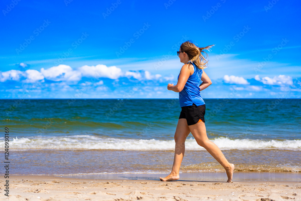 Beautiful middle aged woman training running on sandy beach in summertime. Physical activity on beach. Side view Beautiful middle aged woman training running on sandy beach in summertime. Physical activity on beach. Side view