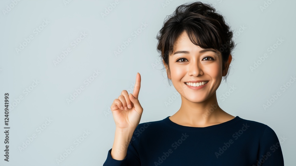 Cheerful japanese businesswoman gesturing upward with index finger, radiating positivity and professional confidence against minimalist gray background Cheerful japanese businesswoman gesturing upward with index finger, radiating positivity and professional confidence against minimalist gray background