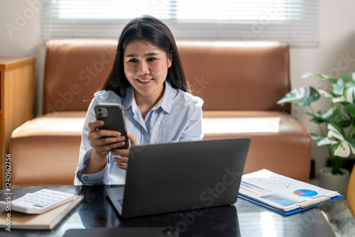 A woman is sitting on a couch with a laptop and a cell phone in front of her