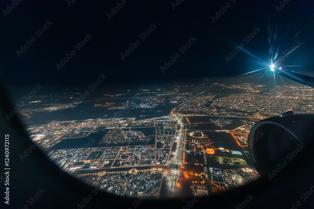 Airplane engine and wing flying over a big illuminated city at night, seen through an aircraft window
