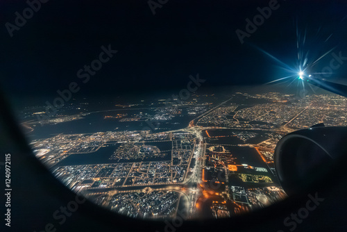 Obraz na płótnie Airplane engine and wing flying over a big illuminated city at night, seen through an aircraft window w salonie
