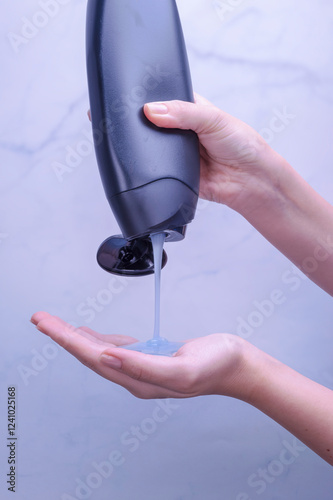 Shower gel in white bottle poured into woman palm