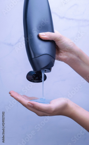 Shower gel in black bottle poured into woman palm