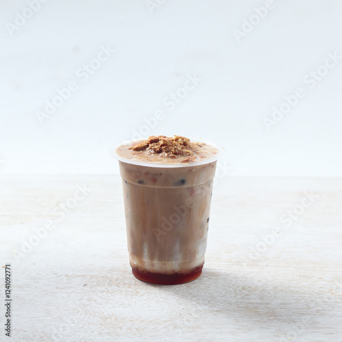 A creamy iced drink with a layer of crunchy topping sits invitingly on a light wooden surface, ideal for cooling off on a warm day