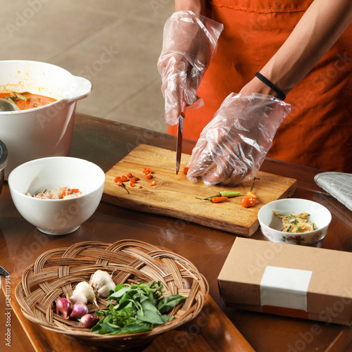 A culinary expert skillfully chops vegetables and herbs on a wooden board while surrounded by fresh ingredients and prepared sauces