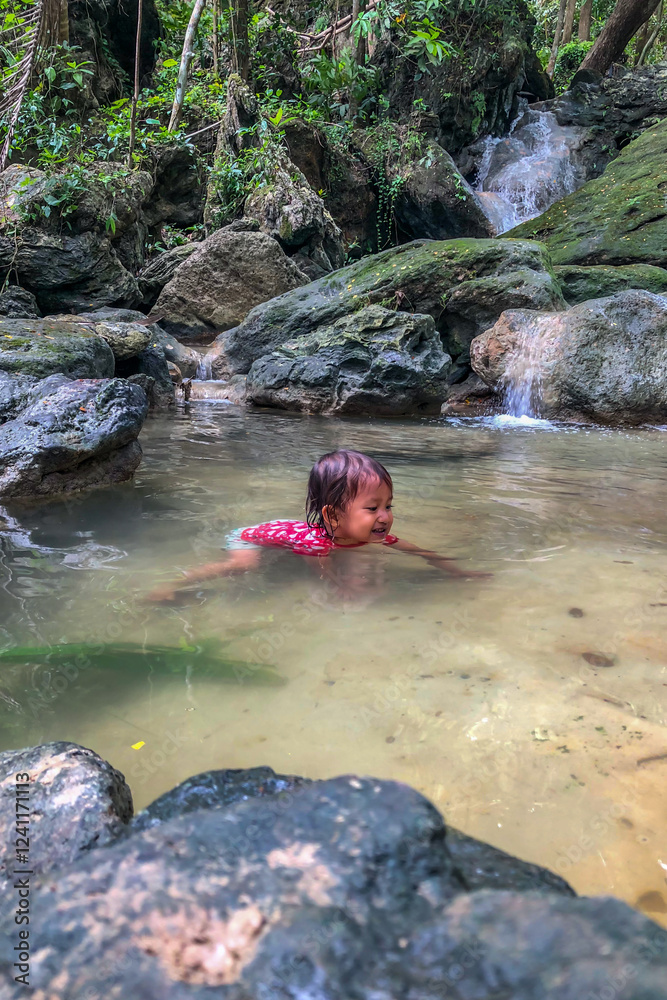 little asian girl playing by the waterfall with a heart full of laughter.