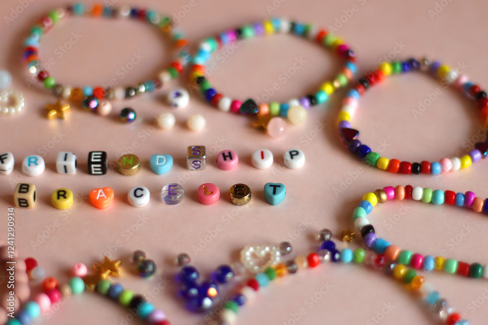 Friendship bracelet spelled with letter beads. Colorful handmade bracelets and various beads. Selective focus, pink background.