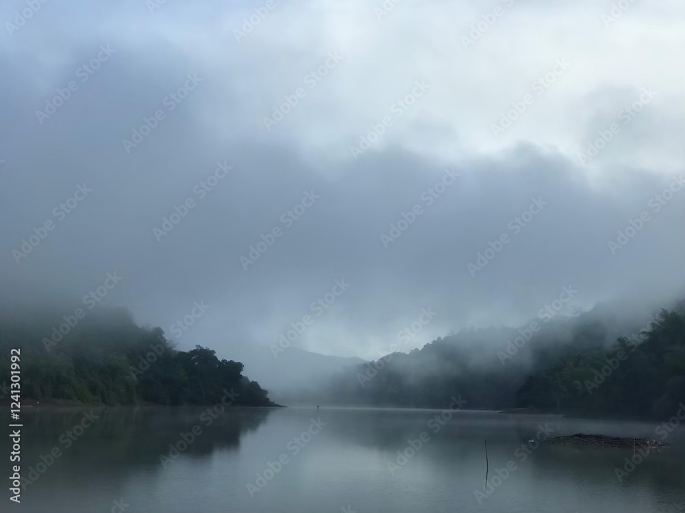 “Mystical Mist Over a Tranquil River: A serene morning scene featuring a calm river shrouded in thick mist, surrounded by lush green hills fading into the fog. The stillness of the water reflects the “Mystical Mist Over a Tranquil River: A serene morning scene featuring a calm river shrouded in thick mist, surrounded by lush green hills fading into the fog. The stillness of the water reflects the