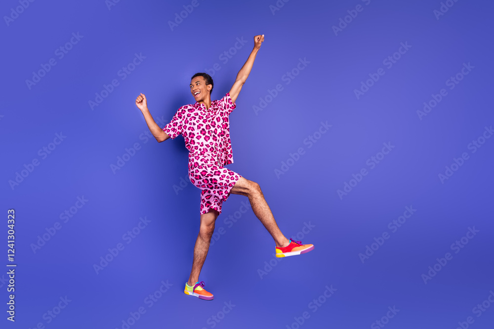 Energetic young man in patterned clothing jumping with joy against a vivid purple backdrop Energetic young man in patterned clothing jumping with joy against a vivid purple backdrop