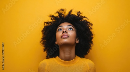 Contemplative young woman with natural black curly hair wearing a bright yellow sweater gazing upward against a vibrant yellow background.
