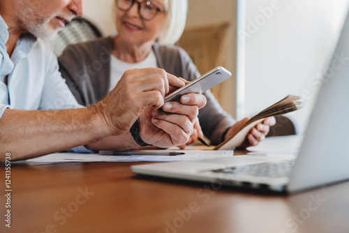 Serious older couple managing planning budget together, reading loan or mortgage documents, mature woman and man checking bills, domestic finances, using laptop, sitting on couch in living room