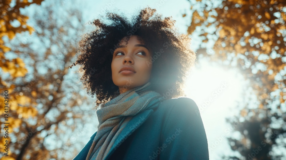 Portrait of young Afro-haired woman wearing teal coat and gray scarf walking in autumn park surrounded by golden leaves on sunny day Portrait of young Afro-haired woman wearing teal coat and gray scarf walking in autumn park surrounded by golden leaves on sunny day