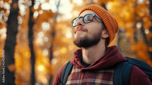 Young man in hipster attire enjoying autumn scenery with golden leaves and a cozy sweater, capturing the essence of fall exploration. photo