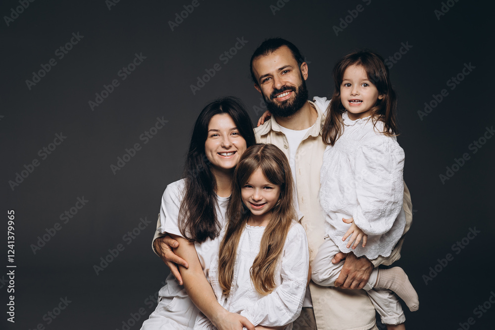 A young sincere family where a stylish bearded father and a cute wife hold their cute children in their arms. Family photo shoot in the studio A young sincere family where a stylish bearded father and a cute wife hold their cute children in their arms. Family photo shoot in the studio