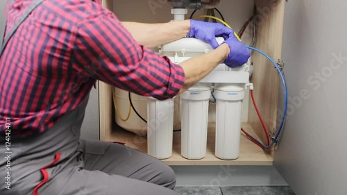 Male plumber installs a reverse osmosis water purification system under the kitchen sink. The concept of clean drinking water.