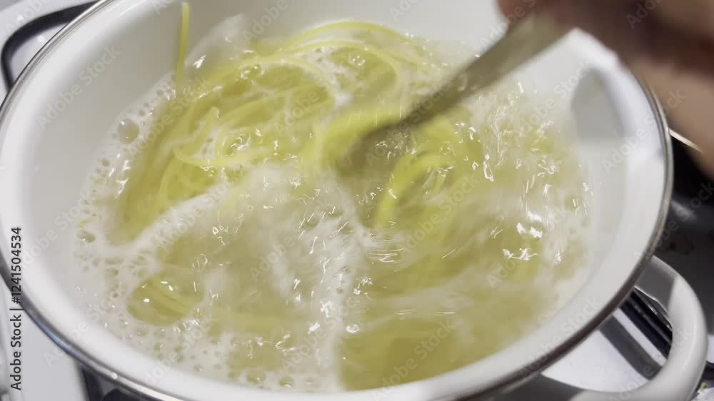 Stir the spaghetti with a spoon in boiling water while cooking in a saucepan. shooting. Stir the spaghetti with a spoon in boiling water while cooking in a saucepan. shooting.