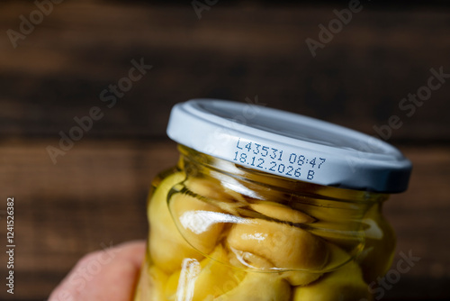 Glass jar of pickled champignon mushrooms with white lid with expiration date, closeup