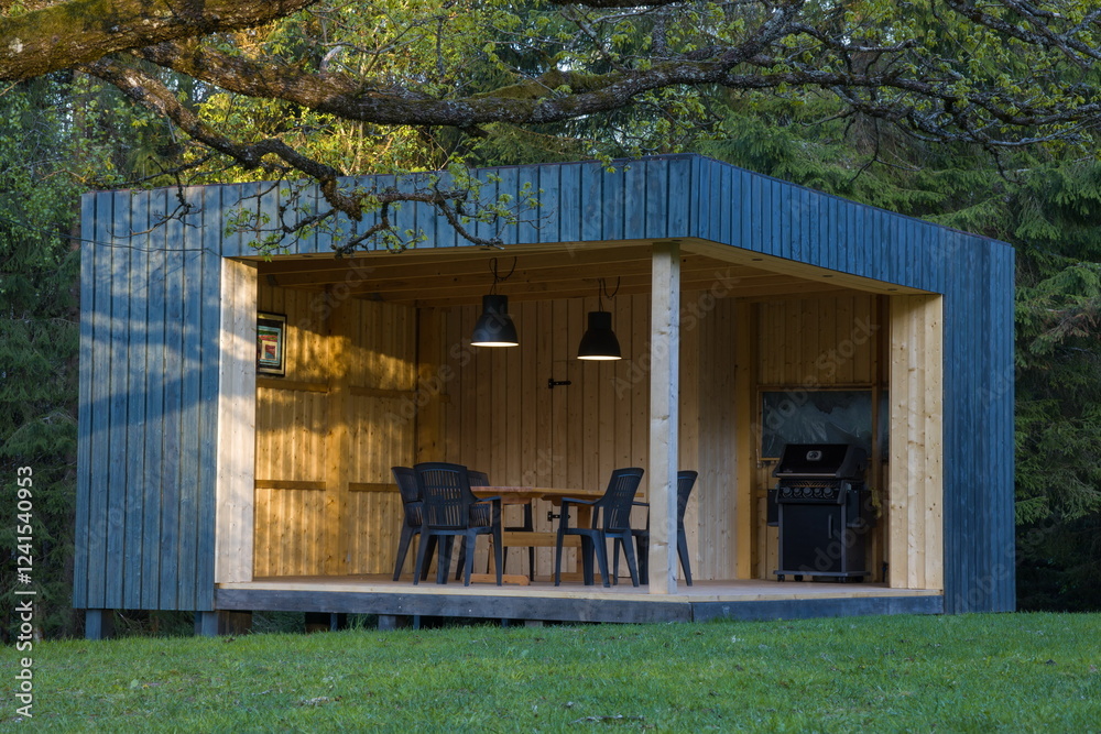 Modern wooden gazebo in a serene forest setting. Contemporary cube design with table and chairs.