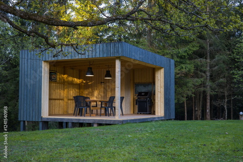 Modern wooden gazebo in a serene forest setting. Contemporary cube design with table and chairs.
