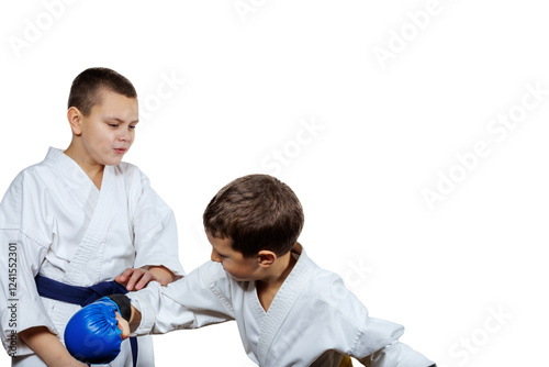 On a white isolated background, a small athlete with a yellow belt in blue pads hits a boy with a blue belt with his hand photo