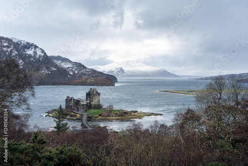 Eilean Donan Castle with bridge under a grey clouded sky and snowy mountains in the background in Scotland photo