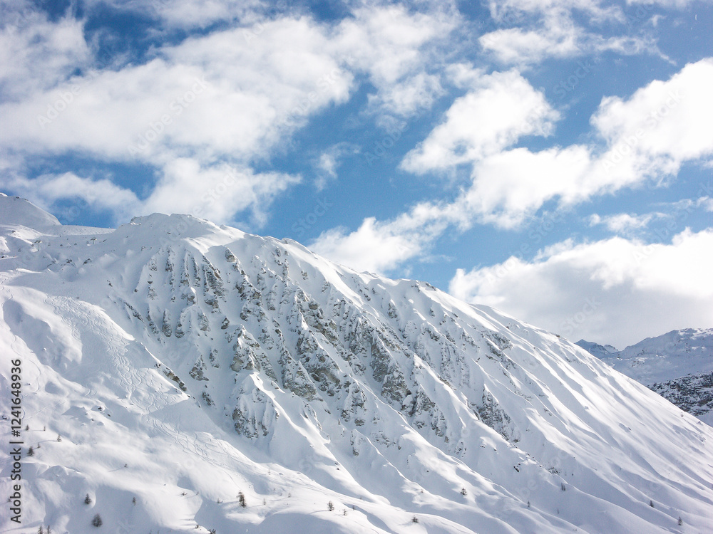 Obraz premium A snowy rocky mountain range and blue sky on a sunny near the ski pistes of a ski resort in the French or Swiss Alps in the winter